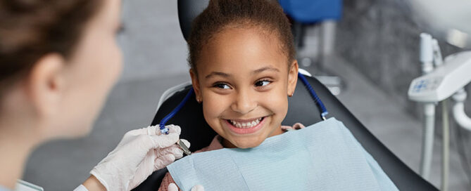 Portrait of smiling little girl in dental chair with nurse preparing her for teeth check up, copy space