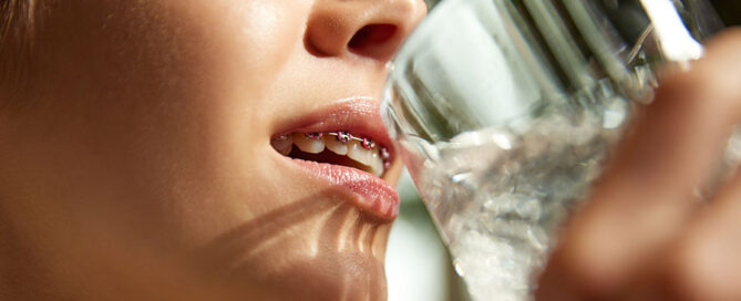 Cropped photo of young woman in braces drinking water. importance of hydration for oral health. Concept of beauty care and medicine, food, nutrition, healthy lifestyle. Ad